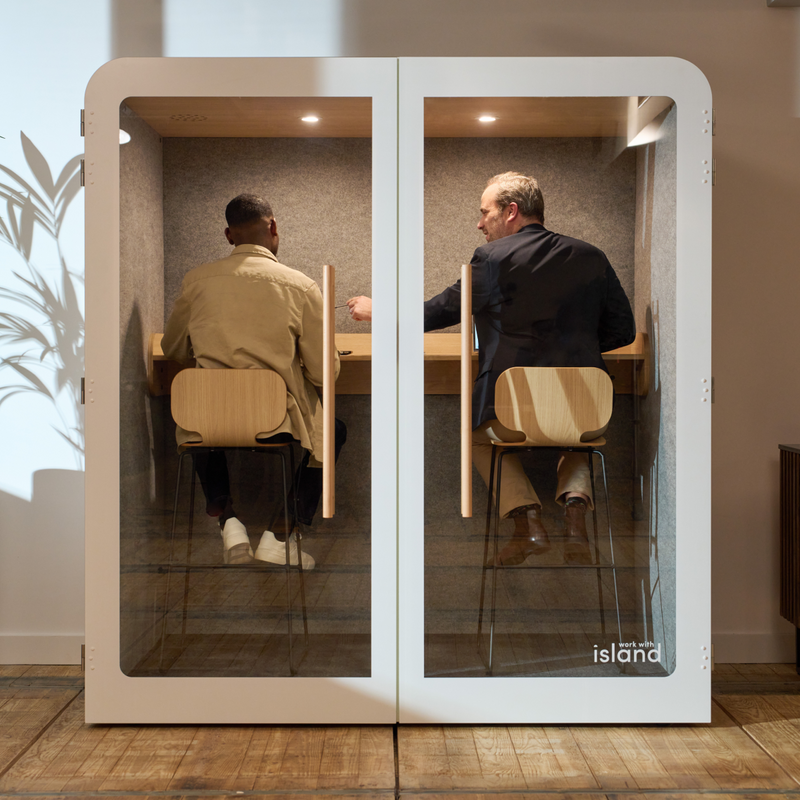 Espace de travail aménagé avec une cabine insonorisée et deux personnes qui travaillent cote à cote