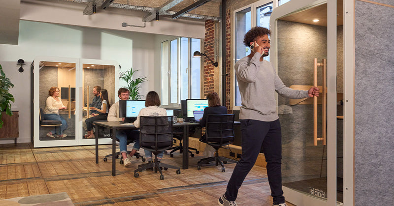 homme au téléphone dans un bureau qui rentre dans une cabine individuelle