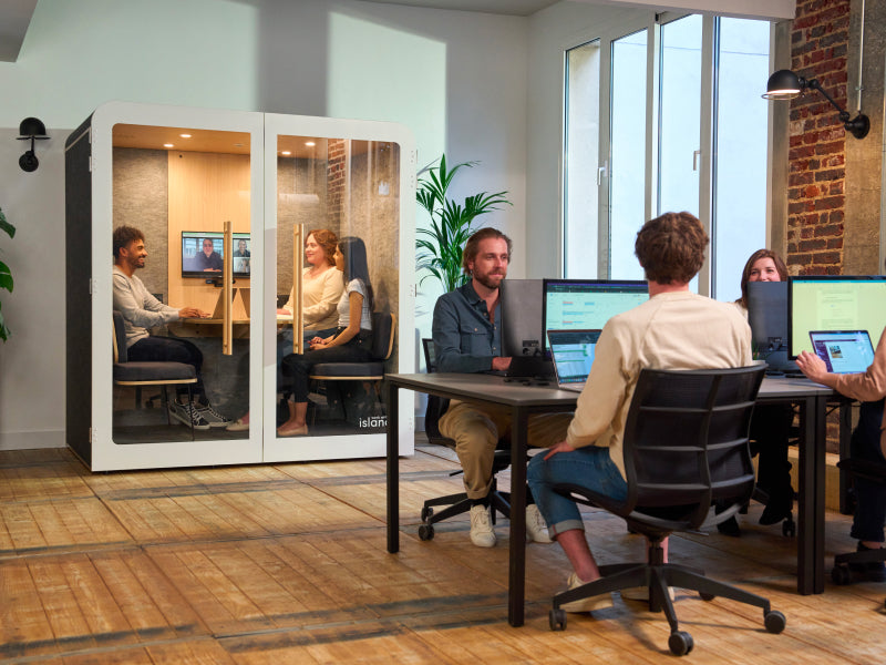 Espace de travail aménagé dans un open space avec une cabine 4 personnes au fond et des individus qui travaillent